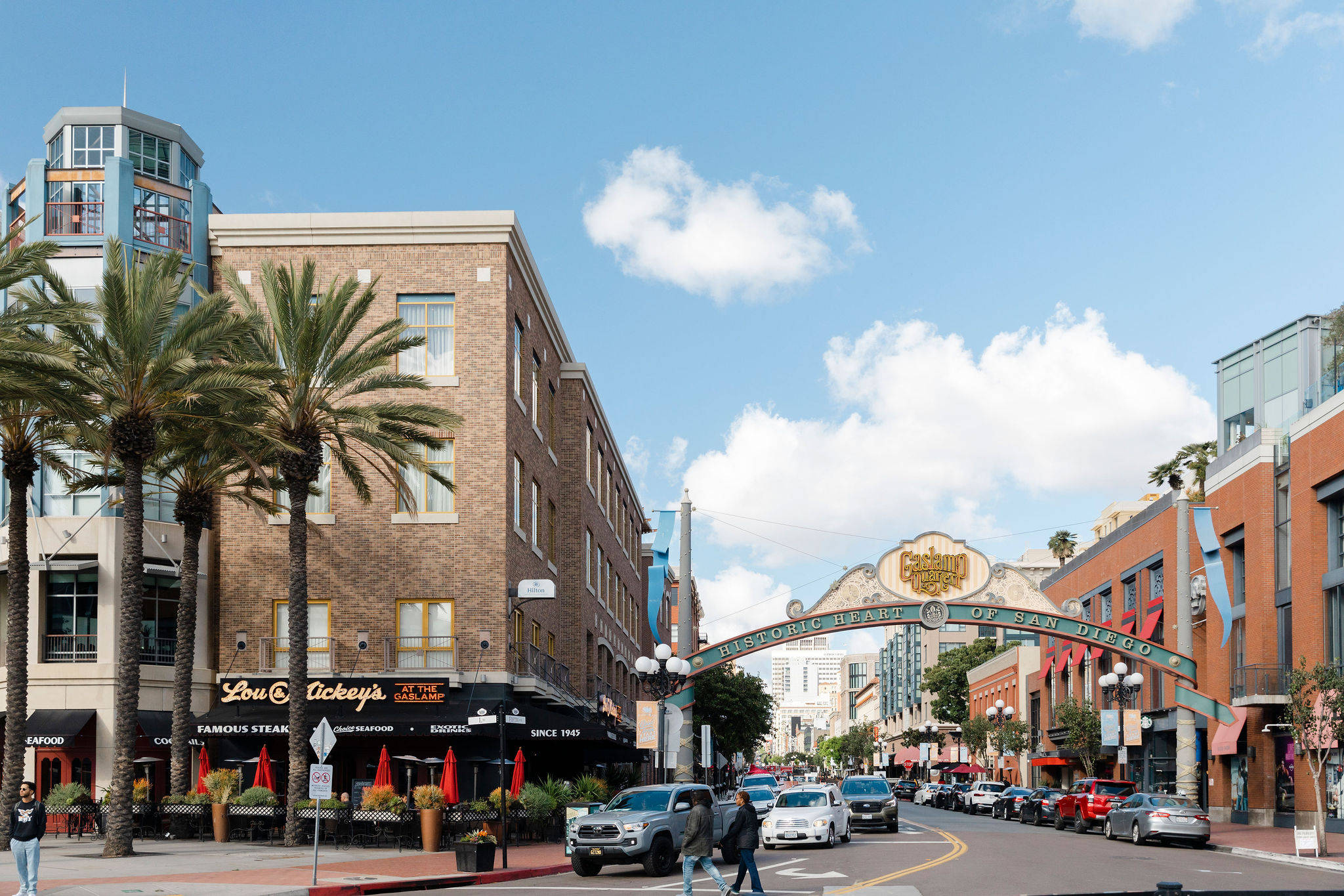 Street scene in San Diego's Gaslamp Quarter with palm trees, shops, cars, and the iconic Gaslamp Quarter archway.