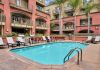 Outdoor apartment pool area with lounge chairs, palm trees, and balconies overlooking the water.