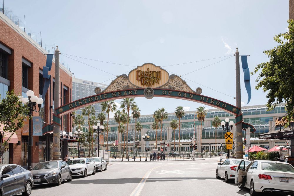 Archway reading "Historic Heart of San Diego" above a sunny street with cars, palm trees, and buildings in the background.