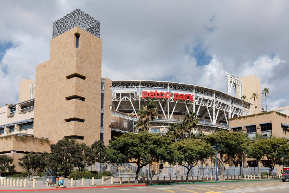 Petco Park baseball stadium in San Diego, with tan stone walls, trees, and a cloudy sky in the background.