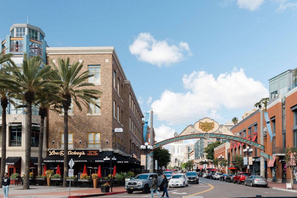 Street scene in San Diego's Gaslamp Quarter with palm trees, shops, cars, and the iconic Gaslamp Quarter archway.